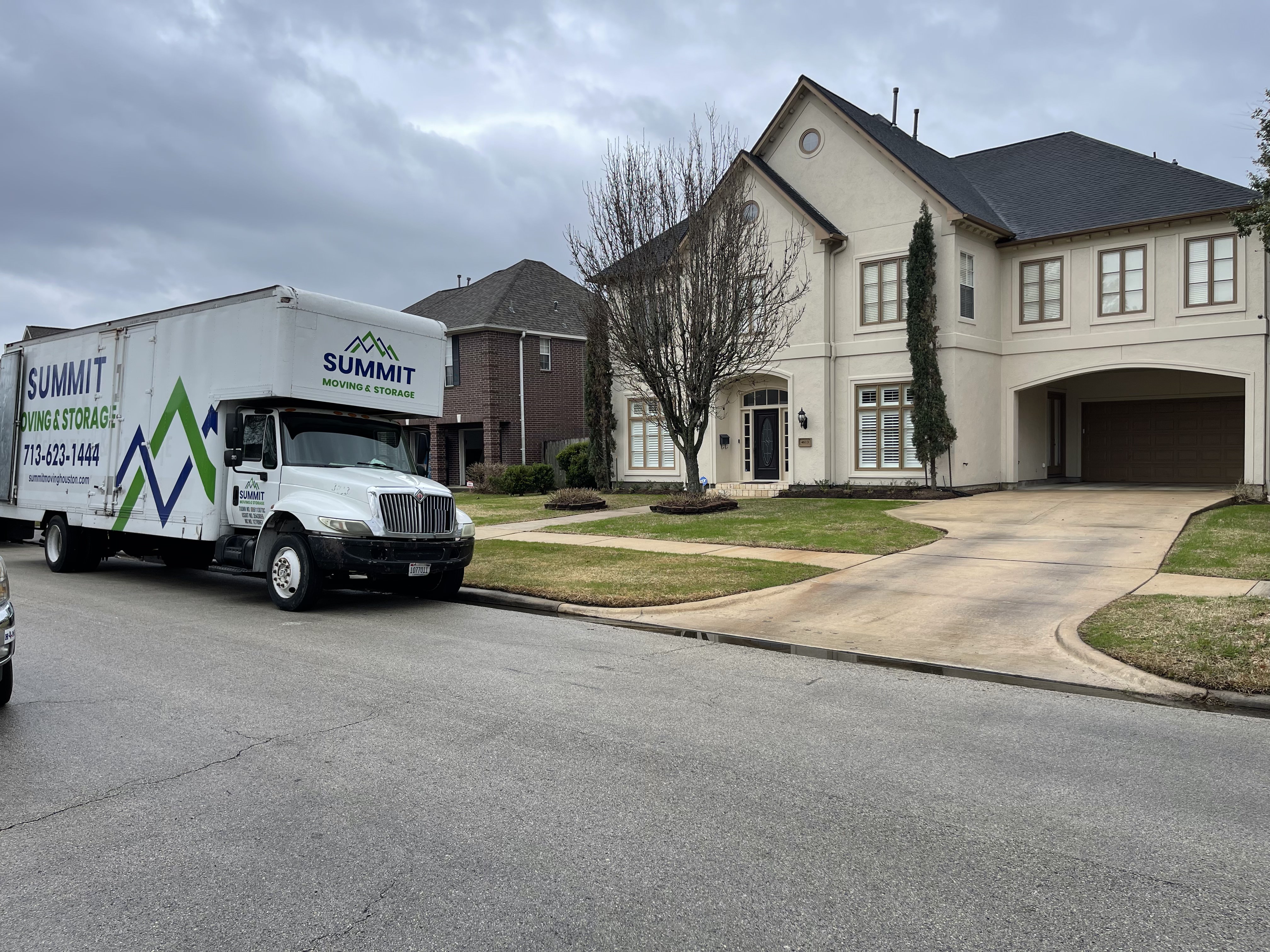 A Summit Moving & Storage truck parked on the street outside a large two-storey suburban home