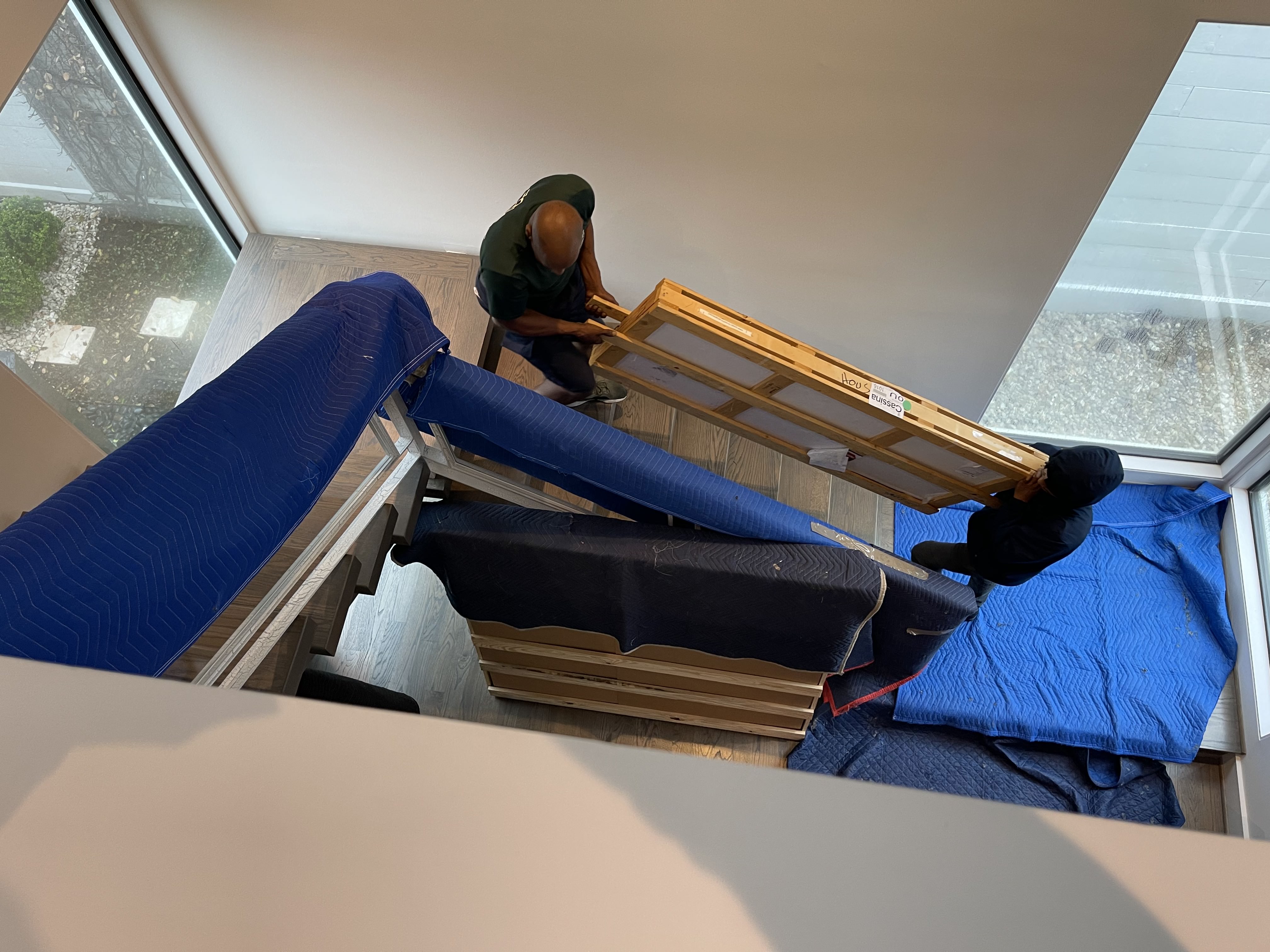 Two Summit Moving crew members carrying a crated table up a flight of stairs in a townhouse in Midtown